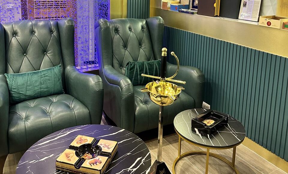 A bright and elegant corner of the MOAT Cigar Lounge in Phuket, featuring green leather armchairs and polished tables.